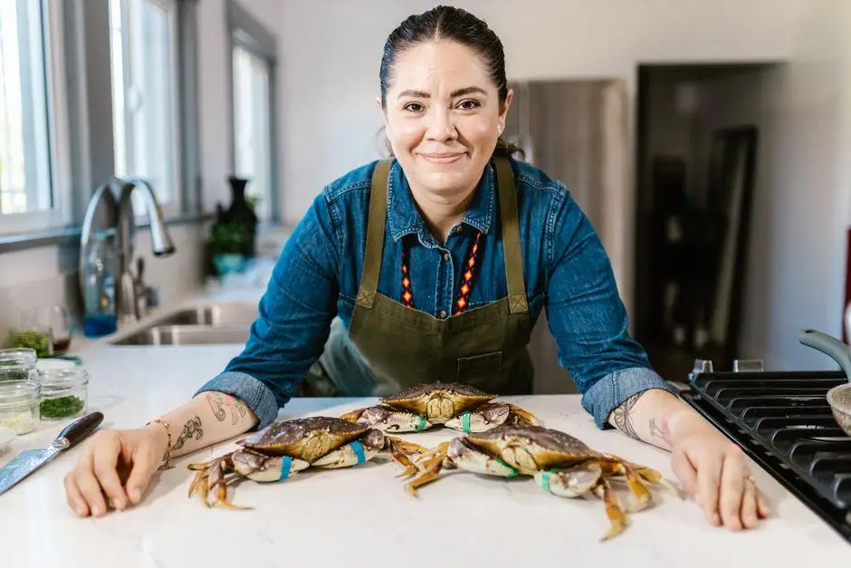 Person in blue shirt and apron with fresh crabs on kitchen counter indoors
